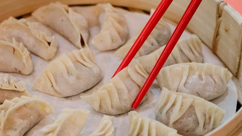 Woman taking raw dumpling with bamboo chopsticks